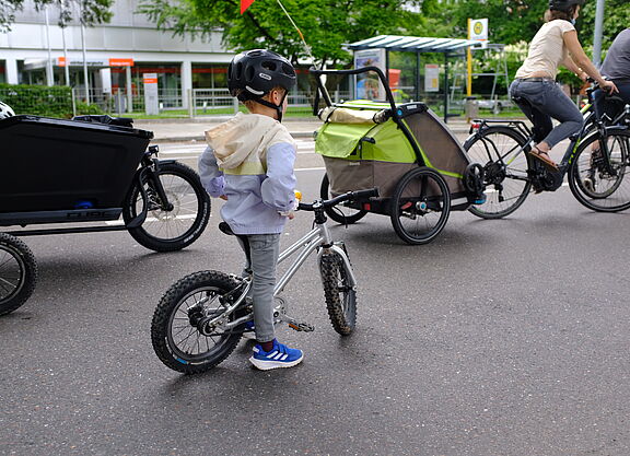 Kidical_Mass_07.2021_copyright_ADFC_BW_oder_Kidical_Mass_Stuttgart__18_. Ein Kind mit Fahrrad und Eltern mit Radanhänger und Lanstenrad sind auf dem Bild zu sehen.