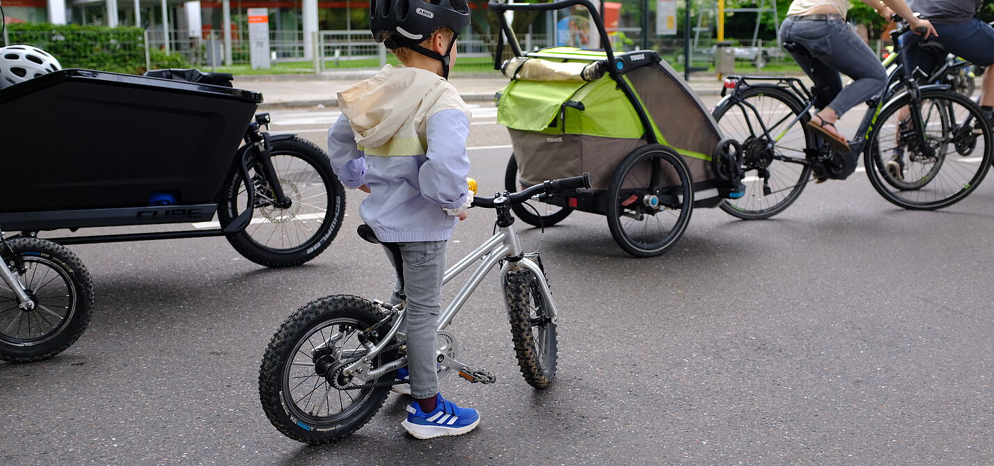 Kidical_Mass_07.2021_copyright_ADFC_BW_oder_Kidical_Mass_Stuttgart__18_. Ein Kind mit Fahrrad und Eltern mit Radanhänger und Lanstenrad sind auf dem Bild zu sehen.